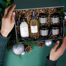 Piotis Naturals large Christmas gift box featuring vegan, natural, and cruelty-free skincare: the One Step Aloe Gel Cleanser, Natural Rosewater Toner, Organic Calming Cream for dry and eczema-prone skin, Metastrophé Anti-Ageing Day Cream, Péplo Anti-Ageing Night Cream with a luxurious rich texture, and Heliaktida Natural Mineral Sunscreen. The box is elegantly wrapped with a black fabric ribbon and presented with festive decorations, including pinecones, greenery, and silver baubles 